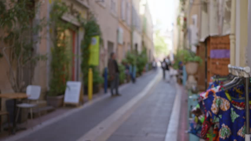 Street view in marseilles with blurred people and colorful textiles on display in a quaint, european alley, evoking a vibrant, urban atmosphere.