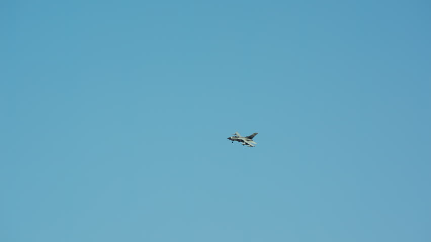 Military fighter jet descending in slow motion against a clear blue sky, preparing for landing with landing gear down during a daytime flight