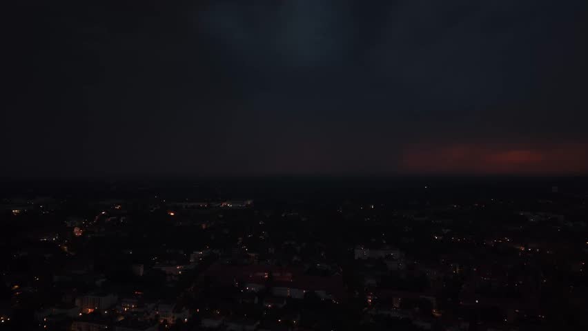 Lightning flash illuminating dark storm clouds above Berlin city lights, showing dramatic weather phenomena and natural power. Beautiful aerial view