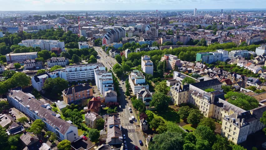 Forward aerial drone shot following a major avenue through the Pontchaillou district in Rennes, France, revealing residential buildings, tree-lined streets and the city skyline in the distance.