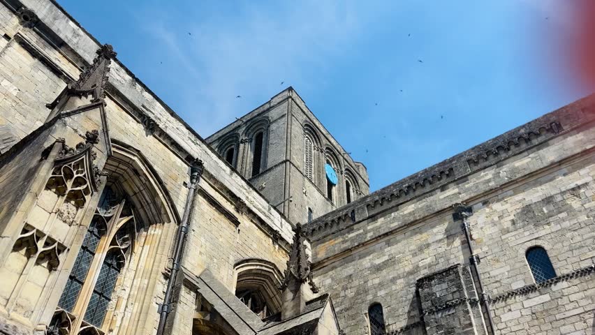 Winchester Cathedral featuring Gothic stone architecture, cathedral tower, arched windows, flying birds, and blue sky in Winchester