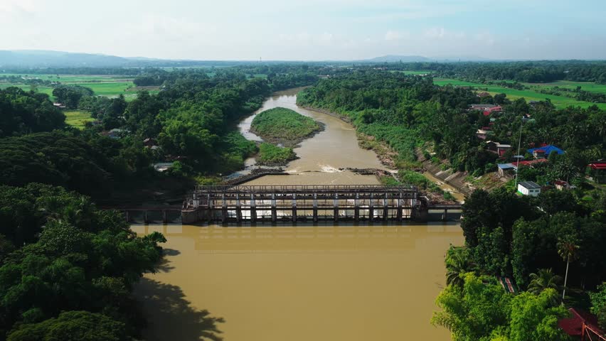 Aerial view of Jalaur Dam spanning the river with lush greenery and rural landscape in Dingle, Western Visayas, Philippines.