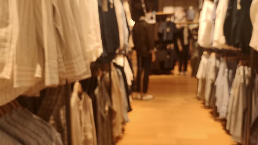 Blurred Defocused Clothing Store Interior with Hanging Shirts and Shoppers Background, Warm Retail Bokeh Backdrop