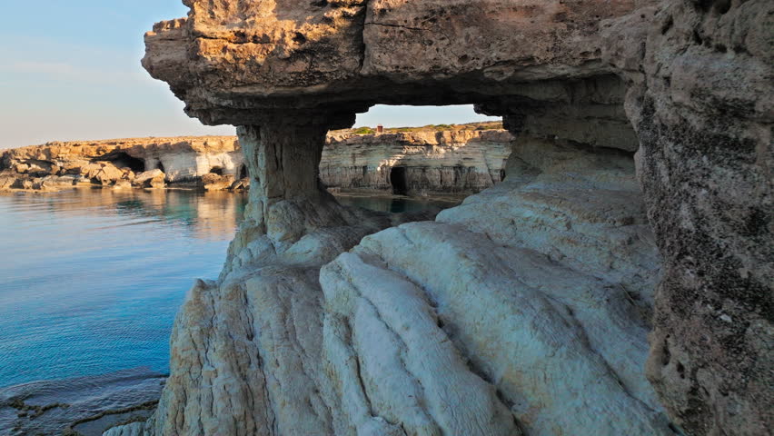 Drone view from inside the Cape Cavo Greco Sea Caves in Cyprus. Natural rock archways and the calm blue sea create a dramatic coastal scene.
