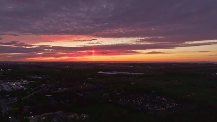 Aerial drone view of Scottish countryside at sunset. Rural villages, farmland and open fields spread beneath dramatic evening sky with glowing horizon