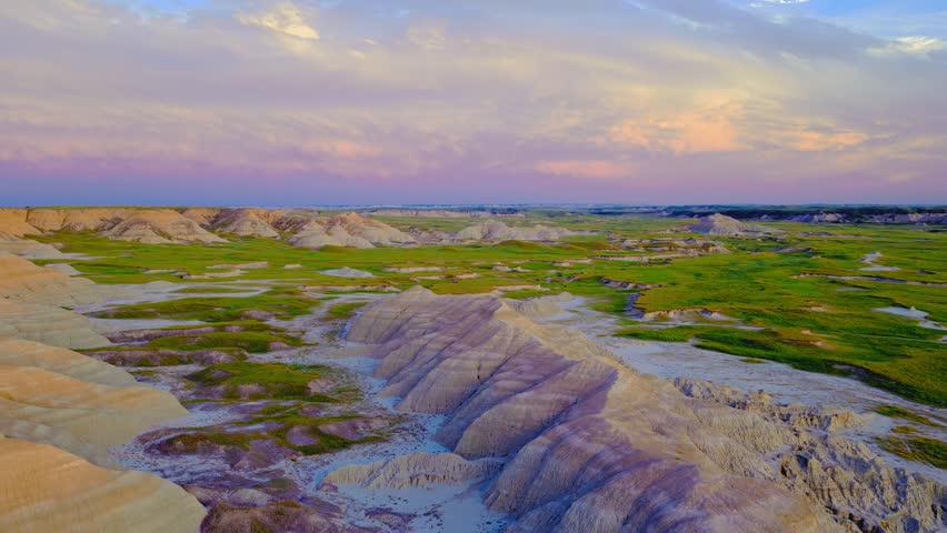 Dramatic drone footage captures golden hour lighting over eroded peaks and lush canyons within South Dakota wilderness. Scenic landscape motion displays majestic geology at dusk.