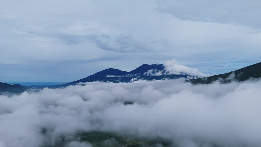 Breathtaking aerial view of a majestic mountain peak surrounded by a thick sea of white clouds under a cool blue sky