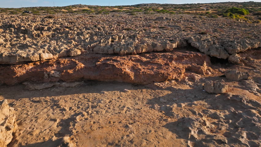 Aerial view of the rocky coastline and sea cave formations at Cape Cavo Greco, Cyprus. The rugged stone landscape meets tranquil Mediterranean water.
