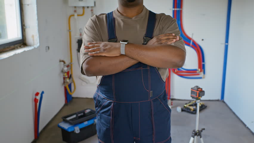 Portrait of African American young adult male plumber standing with arms crossed in house under renovation. Footage suitable for promoting professional plumbing services or home renovation business