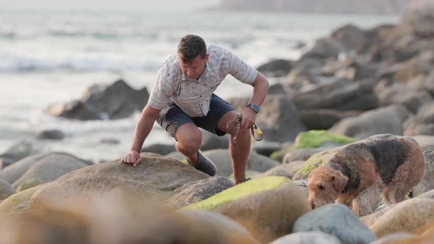 Man plays with dog on rocky beach during sunset in California