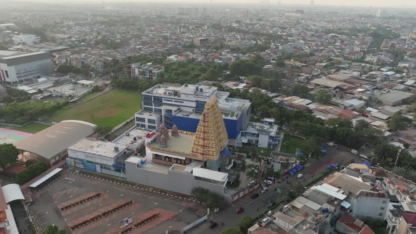 Aerial view of Murugan Temple Jakarta with its distinctive golden gopuram tower surrounded by urban buildings and roads in Kecamatan Kalideres, Daerah Khusus Ibukota, Indonesia.