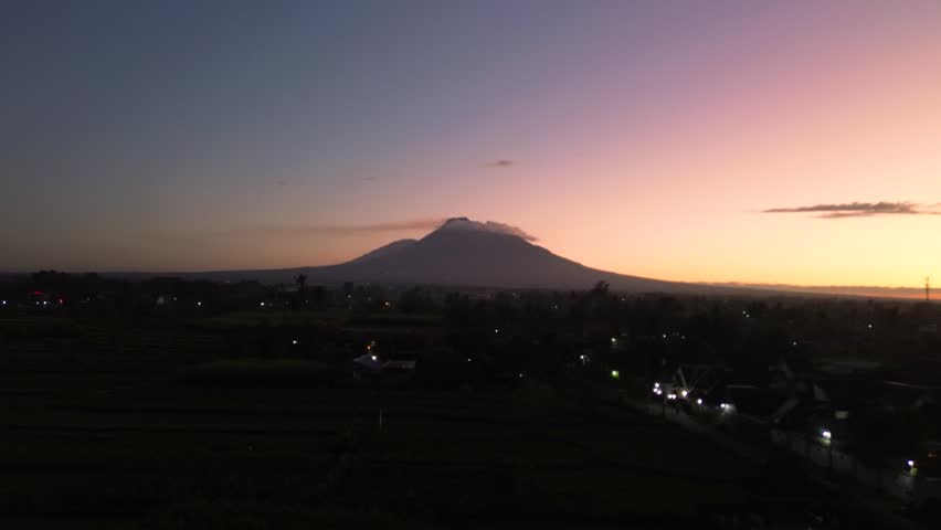 A stunning panoramic view of Mount Merapi from a distance, set against a dark pre-dawn sky. Aerial footage capturing the beauty of Mount Merapi while the sky is still dark.