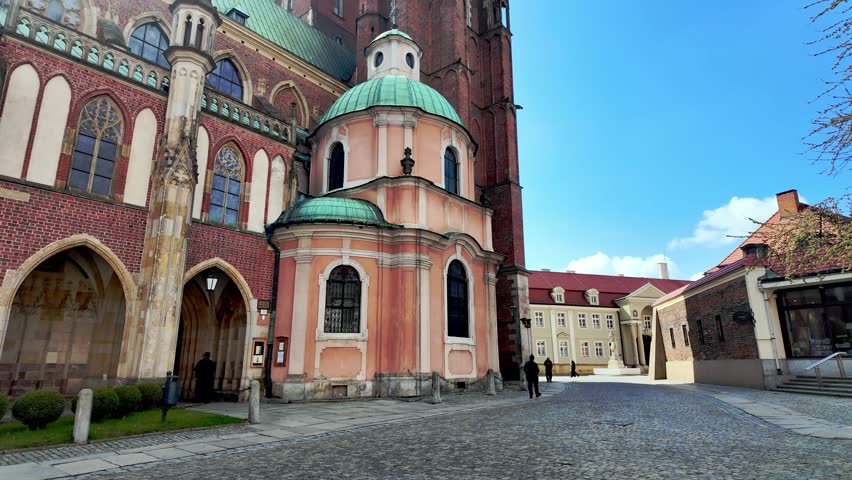 Historic Cathedral of St. John the Baptist on Ostrow Tumski in Wroclaw, gothic red brick facade and baroque chapel, cobblestone street, blue sky, daylight.