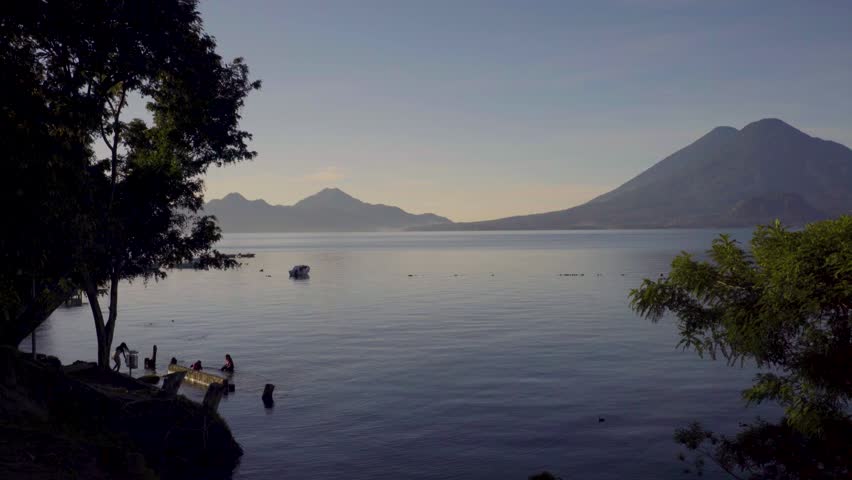 Lake Atitlan morning, people by shore, serene water, volcanoes.