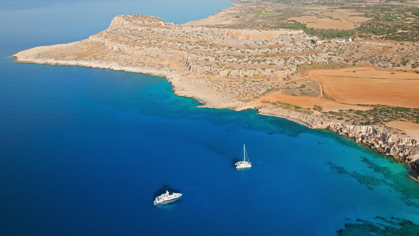 Drone view of Cape Cavo Greco bay and coastline in Cyprus. A boat on the calm sea adds a peaceful travel atmosphere.