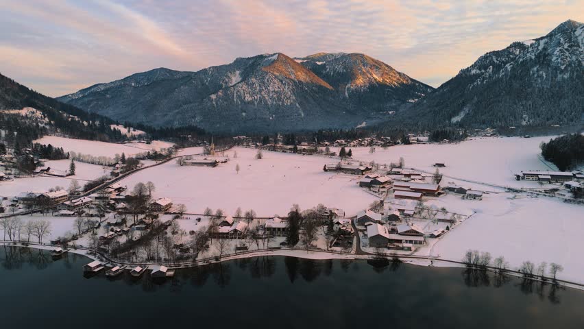 Snow covered village, dark lake water and alpine mountain peaks at sunset in Schliersee, Bavaria aerial.