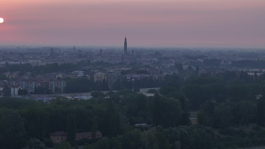 Cremona skyline rises across Cremona, Lombardy, Italy, with Torrazzo, Cremona Cathedral and historic church bell towers above the city beneath evening haze, drone forward flyover.