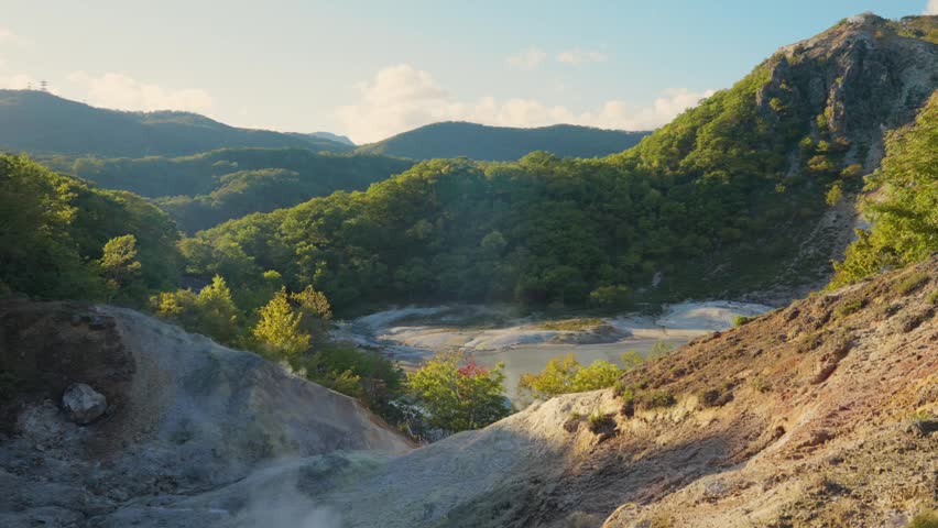Picturesque landscape view of a volcanic valley with steam rising from geothermal hot springs at Jigokudani Hell Valley, a famous onsen resort area located in Noboribetsu, Hokkaido