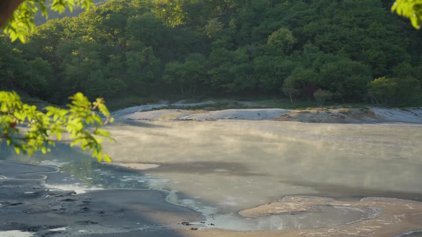 Golden morning light illuminating the natural steam rising from a hot spring pond in the lush green forest of Jigokudani Hell Valley, a famous volcanic caldera in Noboribetsu, Hokkaido, Japan