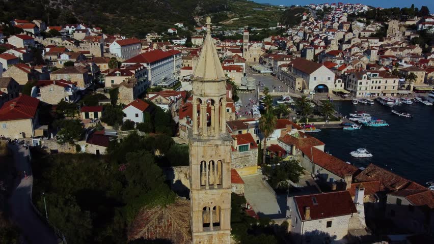 Aerial view of the historic Hvar Cathedral bell tower surrounded by terracotta rooftops, the bustling harbor, and the Adriatic Sea in Hvar, Split-Dalmatia County, Croatia.