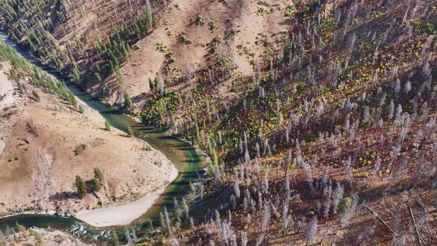 Aerial view of Banks Lowman Road winding along the river, showcasing a contrast between burnt forest and green trees in Garden Valley, Idaho, United States.
