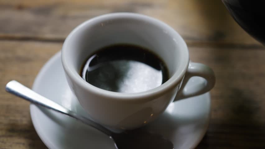 Close up of coffee being poured into a white cup on wooden table.