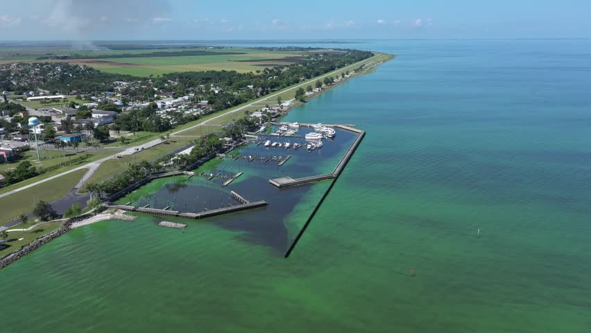 Boats in marina, turquoise water, green algae, aerial view.
