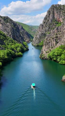 Vertical aerial drone view of Matka Canyon, flying over calm water between the mountains. Tourist boat in Matka Canyon, Skopje, North Macedonia.