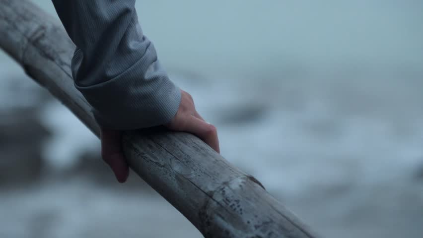 Hand grips rough old bamboo bridge pole by water