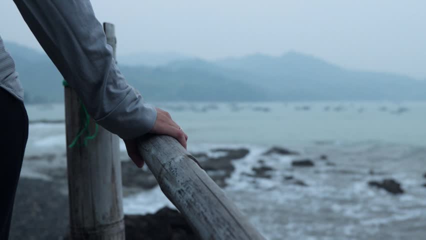 Hand grips rough old bamboo bridge pole by water