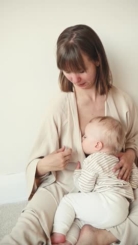 Young mother breastfeeding her toddler daughter while sitting comfortably on the floor in a bright Scandinavian style home.