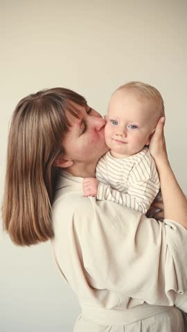 Young mother kissing her one year old daughter on the cheek while holding her in a bright minimalist home filled with natural daylight.