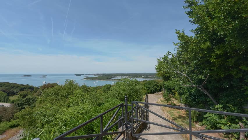 View of the Adriatic coast with lush greenery and a metal railing overlooking the sea in Vrsar, Istria County, Croatia.