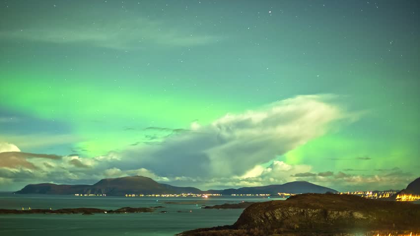View of vibrant green Northern Lights illuminating the night sky above the coastal town of Alesund, More og Romsdal, Norway.