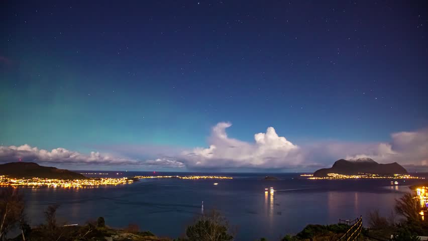 View of the illuminated coastal town of Alesund at night with starry sky and mountains in the background in Alesund, More og Romsdal, Norway.