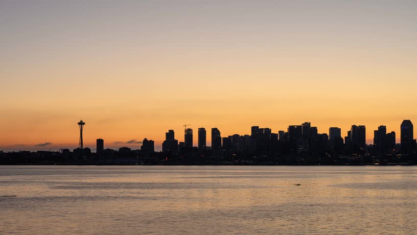 View of the Seattle skyline with the Space Needle silhouetted against a vibrant sunset sky over Elliott Bay in Seattle, Washington, United States.