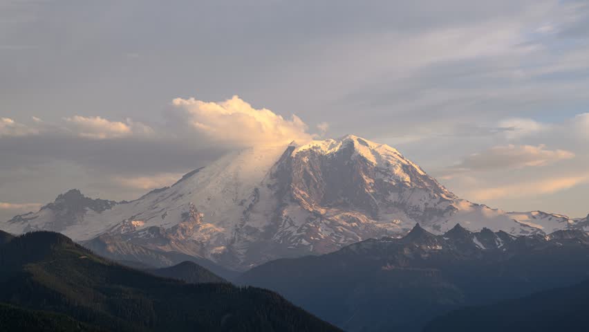 View of Mount Rainier with snow-capped peaks and clouds at sunset in Pierce County, Washington, United States.