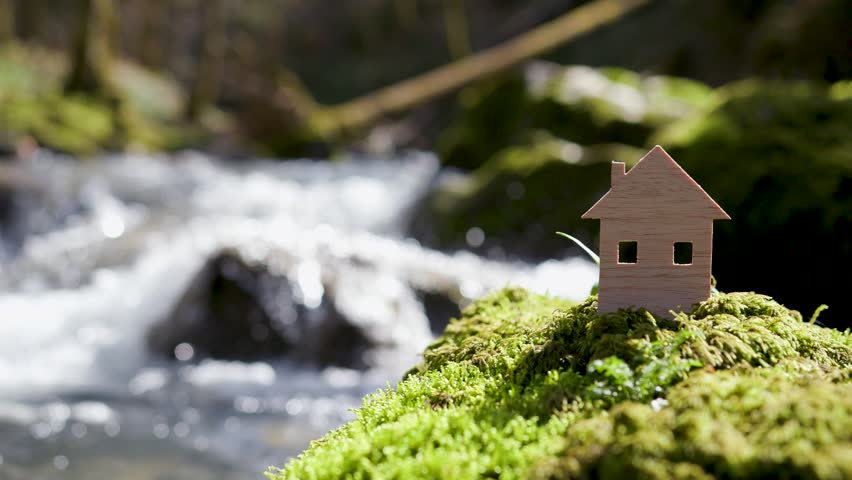 Beautiful sunny house wooden cutout on mossy rock by the river.