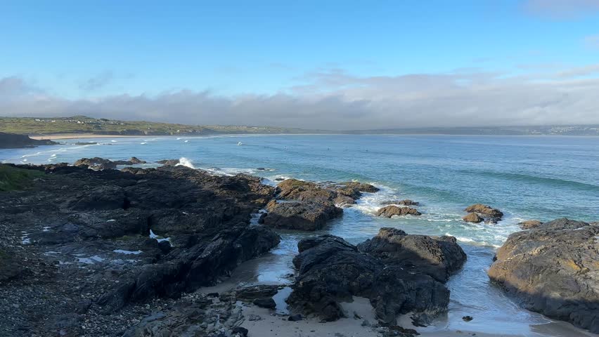 Rocky seashore with gentle ocean waves washing over coastal rocks. Scenic seaside landscape with clear blue water and natural coastal scenery.