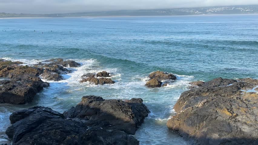 Rocky seashore with gentle ocean waves washing over coastal rocks. Scenic seaside landscape with clear blue water and natural coastal scenery.