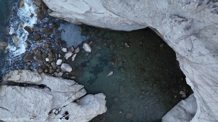 A group of people enjoys swimming and exploring in a rocky area close to the ocean. The sun shines as they navigate the clear waters and the rocky shore.