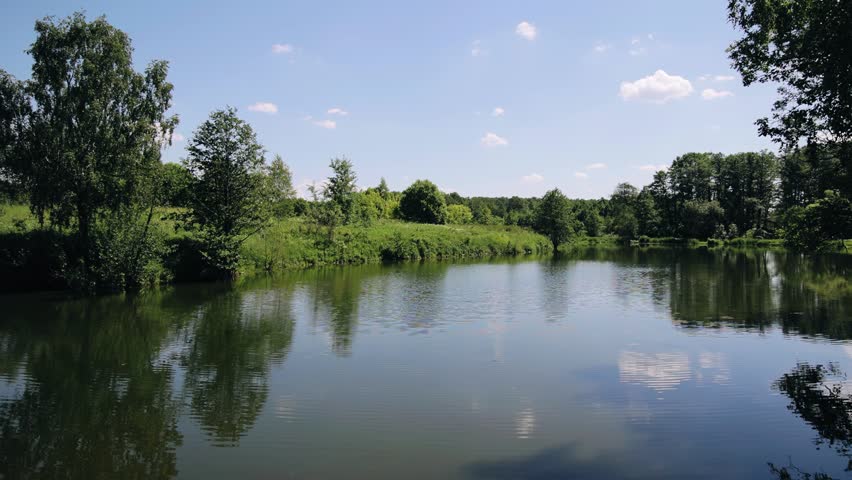 A small picturesque pond in the middle of a forest area. Trees are reflected on the water and ripples from the wind are visible.