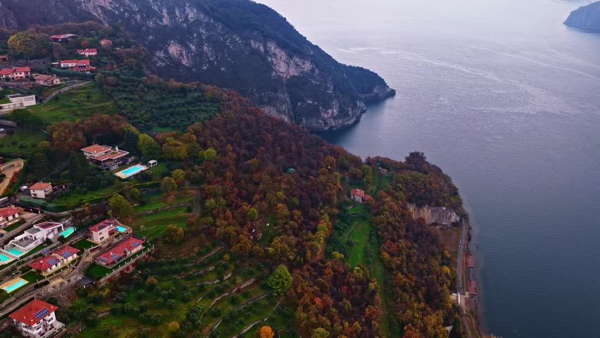 Aerial view of hillside houses, lush trees, and a coastal road along the lake in Italy.