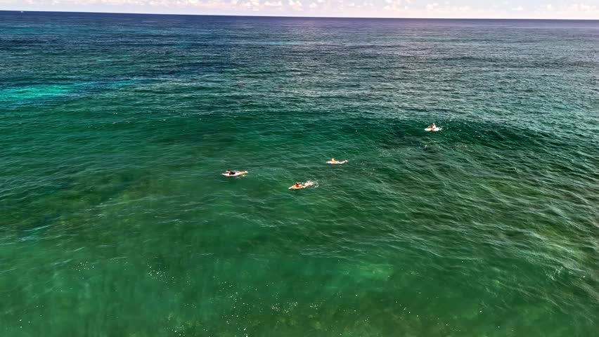 Aerial view of surfers paddling on their boards in the clear turquoise ocean waters off the coast of Bali, Indonesia.