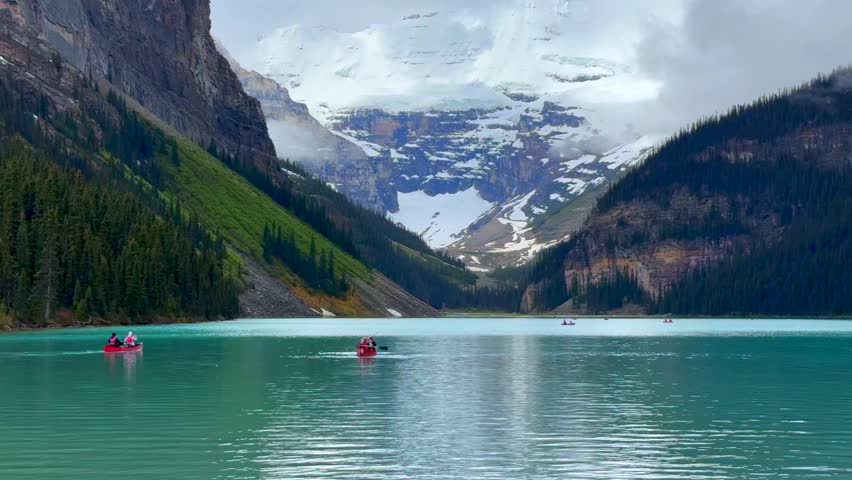 Beautiful view of the lake Louise, Banff Canada. A group of individuals paddles canoes across a turquoise lake surrounded by majestic mountains and lush forests, showcasing the serene beauty of nature