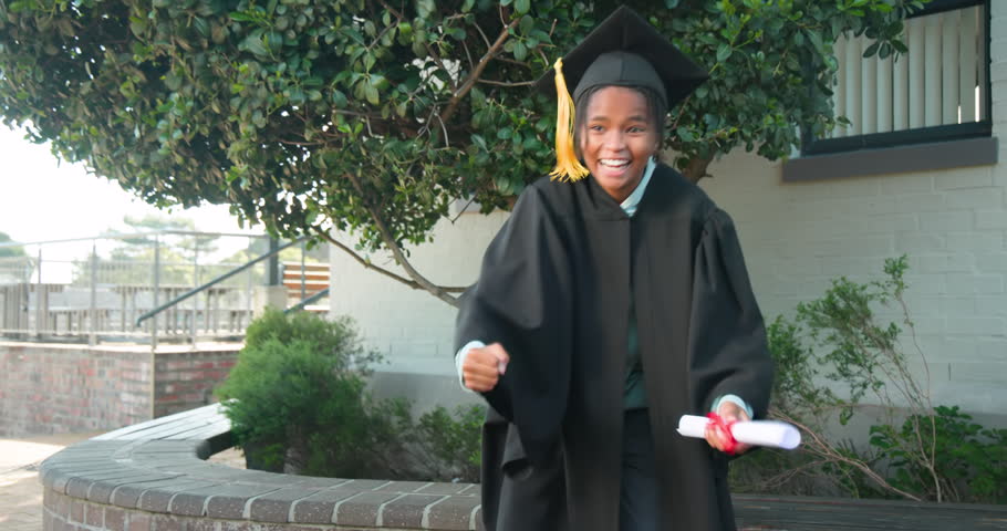 African teen male in gown holding diploma celebrating, pumping fists and tossing cap on campus. Student, graduation, outdoor, celebration, achievement, tassel, tree