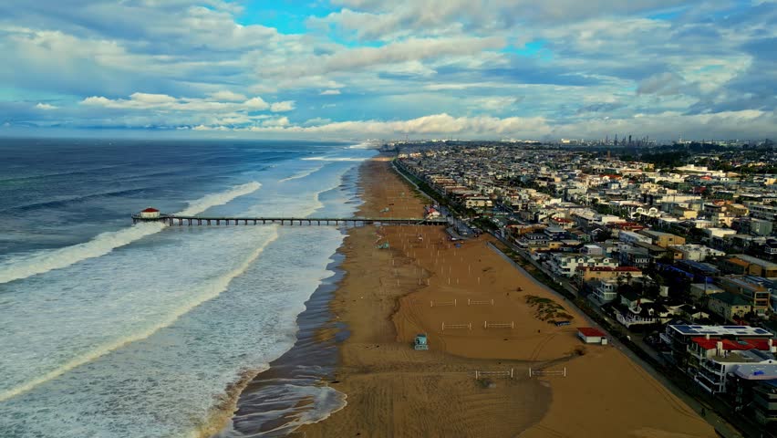Aerial view of the coastline featuring a long pier extending into the ocean, sandy beach, and urban development along the shore in Los Angeles, California, United States.