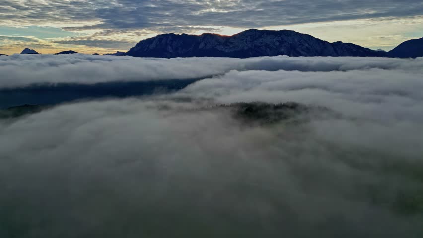 Aerial view of the thick sea of clouds covering the Attersee landscape with distant mountains under a dramatic cloudy sky in Vocklabruck District, Upper Austria, Austria.