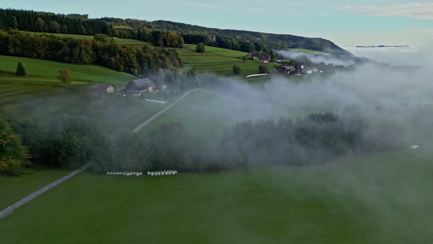 Aerial view of the Attersee region with rolling green hills, scattered rural houses, and low-hanging morning fog over the landscape in Vocklabruck District, Upper Austria, Austria.
