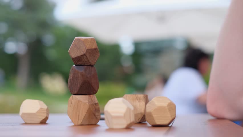 Man placing a wooden Tumi Ishi balancing block on a tower in a Japanese garden, close up